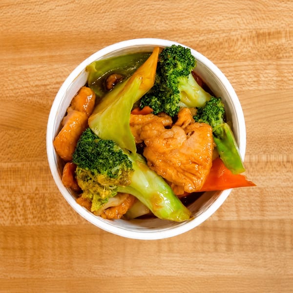 Overhead view of a white bowl filled with chicken, broccoli, and other vegetables in sauce.