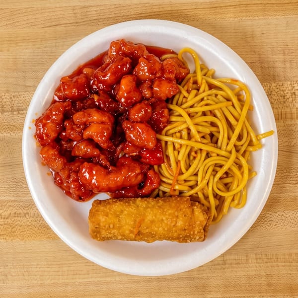 A takeout plate with orange chicken, lo mein noodles, and a crispy egg roll on a wooden table.
