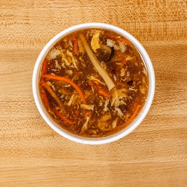 Overhead view of a bowl of hot and sour soup with carrots, mushrooms, and egg on a wooden table.